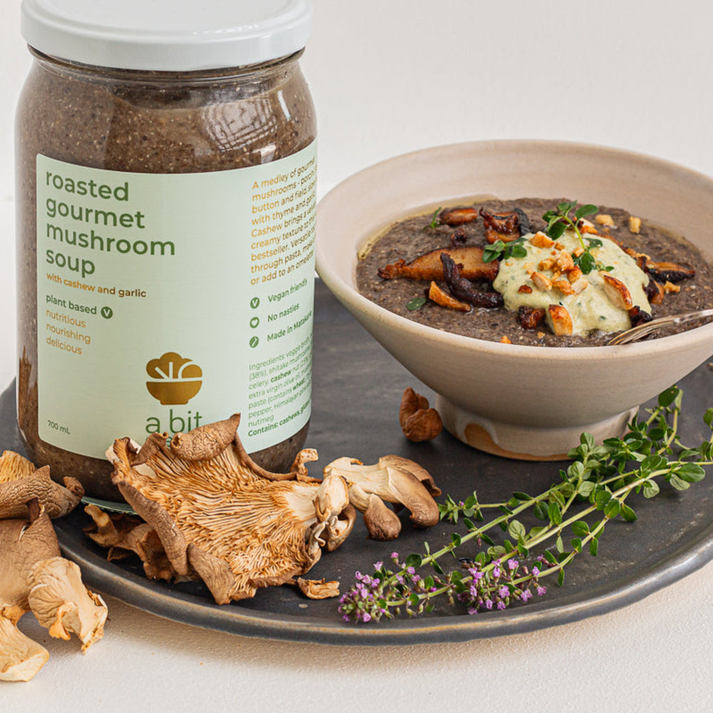 Jar of roasted gourmet mushroom soup with a bowl of soup and mushrooms on a white background