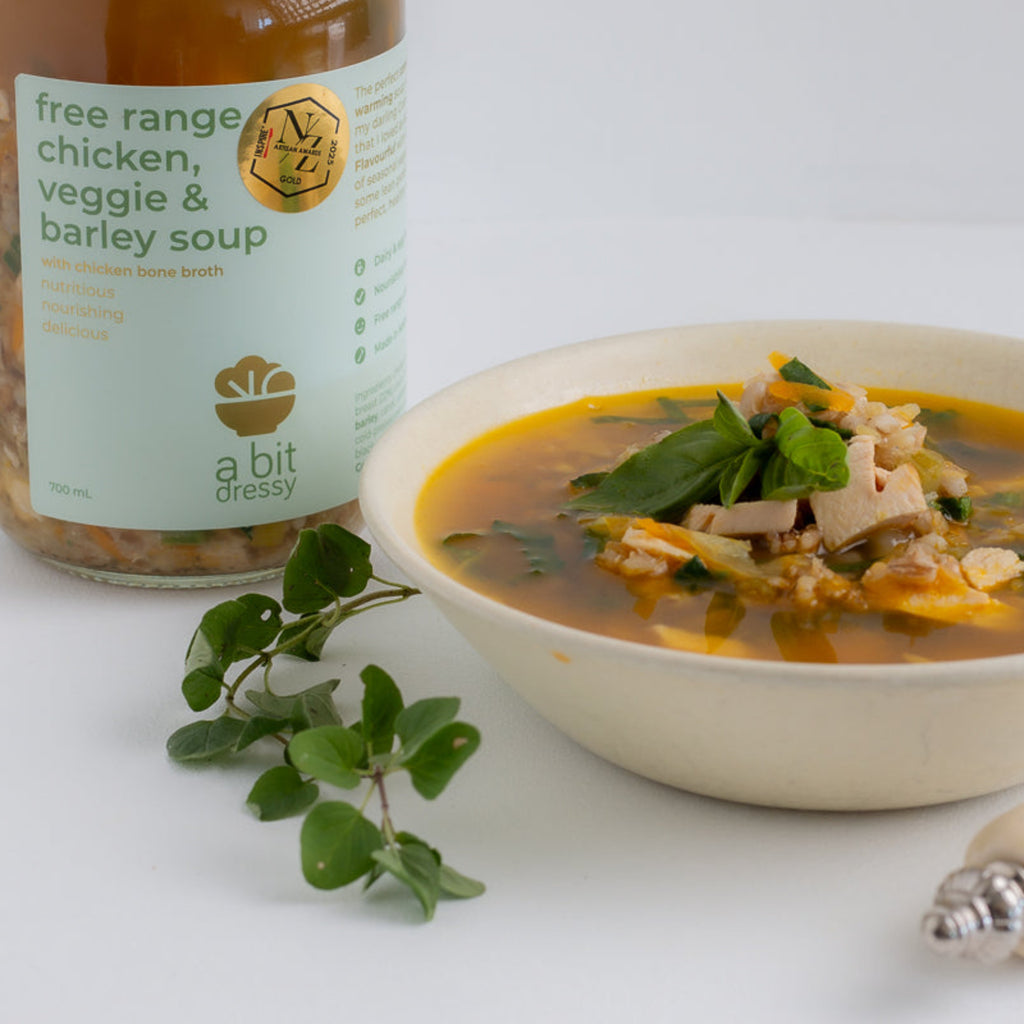 Bowl of soup with a jar of free range chicken, veggie, and butter soup on a white background