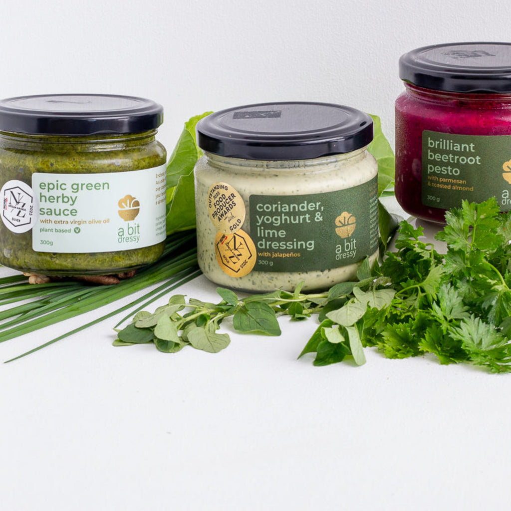Jar of 'epic green herby sauce' on a wooden surface with herbs in the background