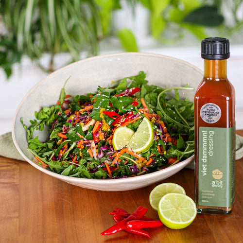 Bowl of salad with a bottle of dressing on a wooden table