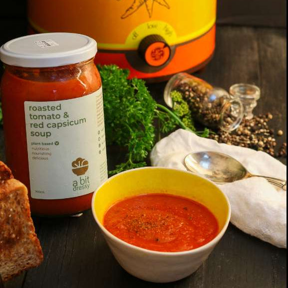 Roasted tomato and red capsicum soup with ingredients and a canister on a dark background.