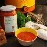 Roasted tomato and red capsicum soup with ingredients and a canister on a dark background.