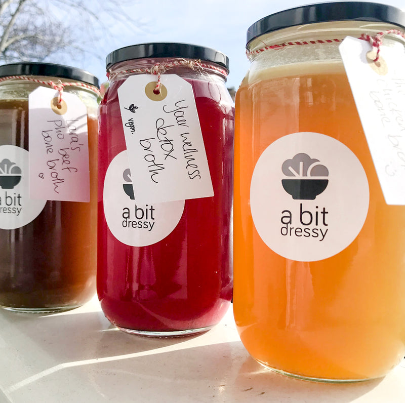 A trio of broths in glass jars, featuring 'Wellness Detox Broth,' 'Chicken Bone Broth,' and 'Veggie Broth,' each jar displaying a unique and savory broth variety designed for different culinary and dietary preferences.