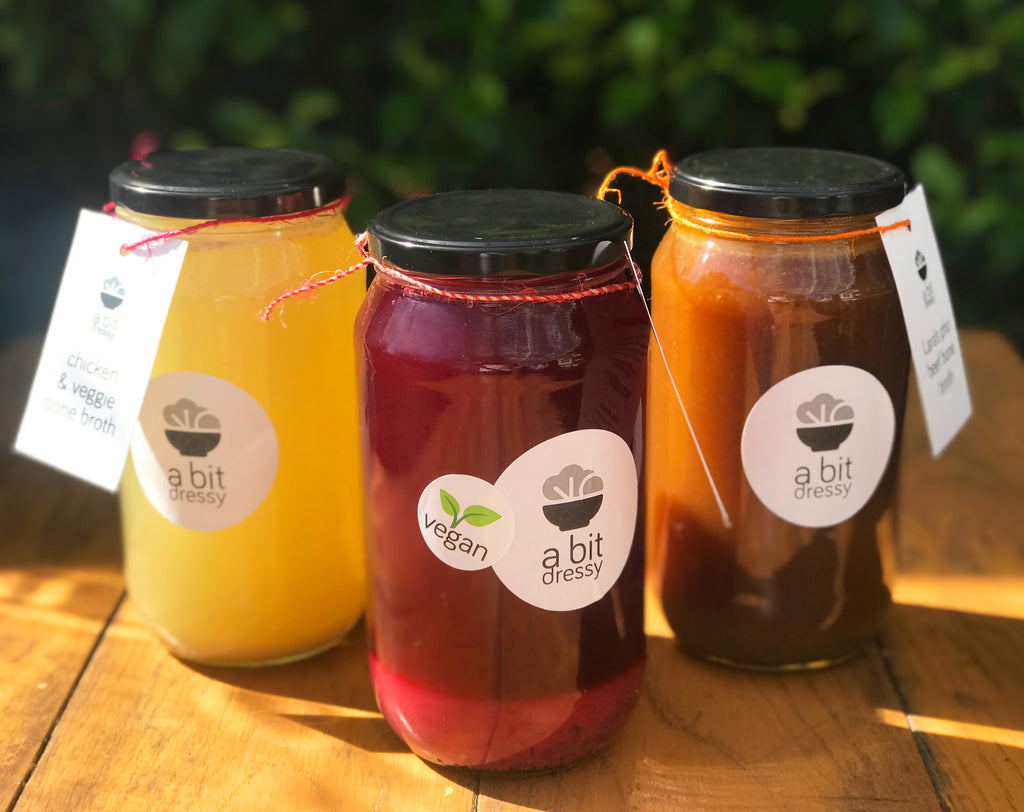A trio of broths in glass jars, including a 'Wellness Detox Broth,' a 'Chicken Bone Broth,' and a 'Veggie Broth,' each offering a unique flavor and health profile