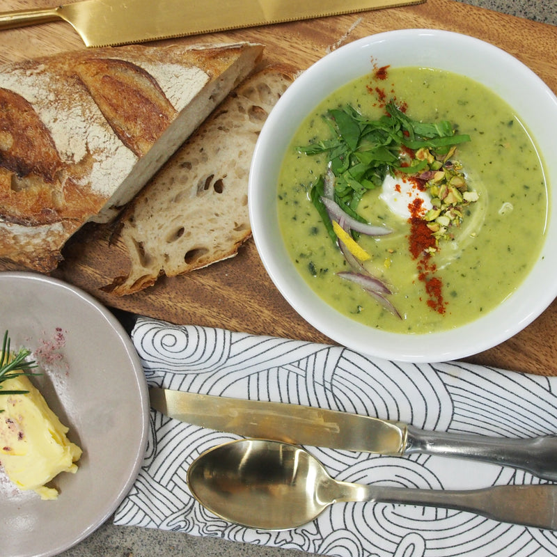 A bowl of creamy potato soup placed on a table, accompanied by slices of bread and a dish of butter, creating a comforting and inviting meal setting