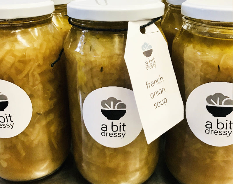 A display of A Bit Dressy's French Onion Soup in glass jars, showcasing a rich and flavorful soup with caramelized onions and a savory broth.