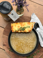 Flat lay image of a delectable French onion soup, with a golden-brown, bubbling cheese crust on top and a slice of toasted bread placed beside it, all elegantly presented on a table.