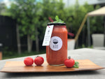 A bottle of Roasted Tomato, Capsicum, and Basil Soup placed among a selection of fresh tomatoes, highlighting the soup's key ingredients and rich flavors.