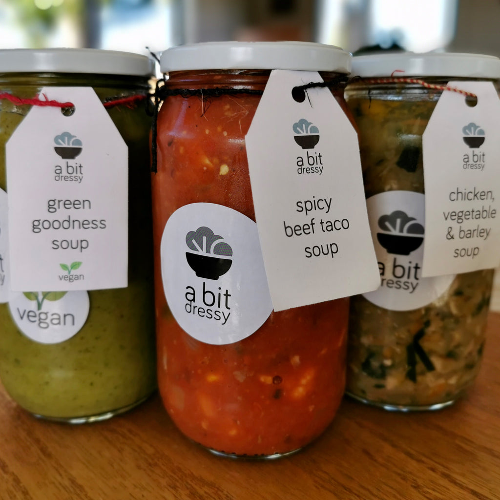 A trio of soups in glass jars, featuring Green Goddess soup, Spicy Beef Taco soup, and Chicken, Vegetable, and Barley soup, offering a diverse selection of flavorful and hearty soup options.