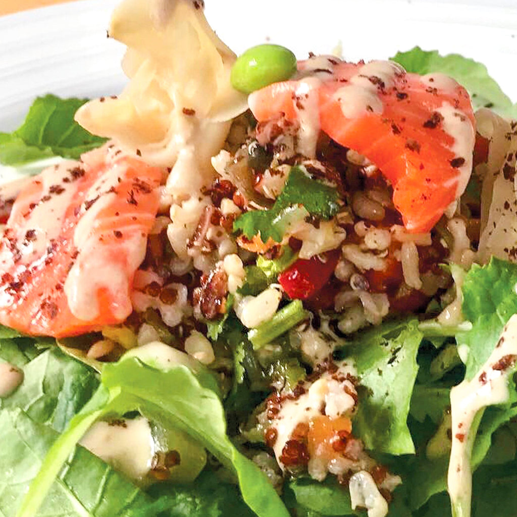 Lara's Umeboshi Goodness Salad Dressing and Marinade being skillfully mixed into a salmon salad, enhancing the flavors of the dish with its unique and tangy and creamytaste.