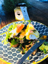 A jar of roasted garlic aioli with extra virgin olive oil beautifully drizzled over Eggs Benedict, with a view of a knife cutting through the dish, highlighting the rich and savory dressing