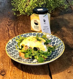 A jar of roasted garlic aioli with extra virgin olive oil artfully drizzled on a plate of Eggs Benedict, adding a rich and savory finishing touch to the classic breakfast dish.