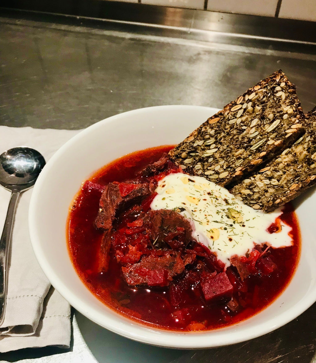 A bowl of Divine Beef Borscht with healthy bread made with beef bone broth, a traditional and hearty soup with vibrant colours and savory ingredients