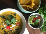 A table set with a bowl of Sweetcorn, Zucchini, Smoked Paprika, and Lime Soup topped with crumbled feta cheese, accompanied by a selection of side dishes and garnishes.