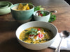 A table set with a bowl of Sweetcorn, Zucchini, Smoked Paprika, and Lime Soup, garnished with crumbled feta cheese, surrounded by a variety of accompaniments and side dishes.