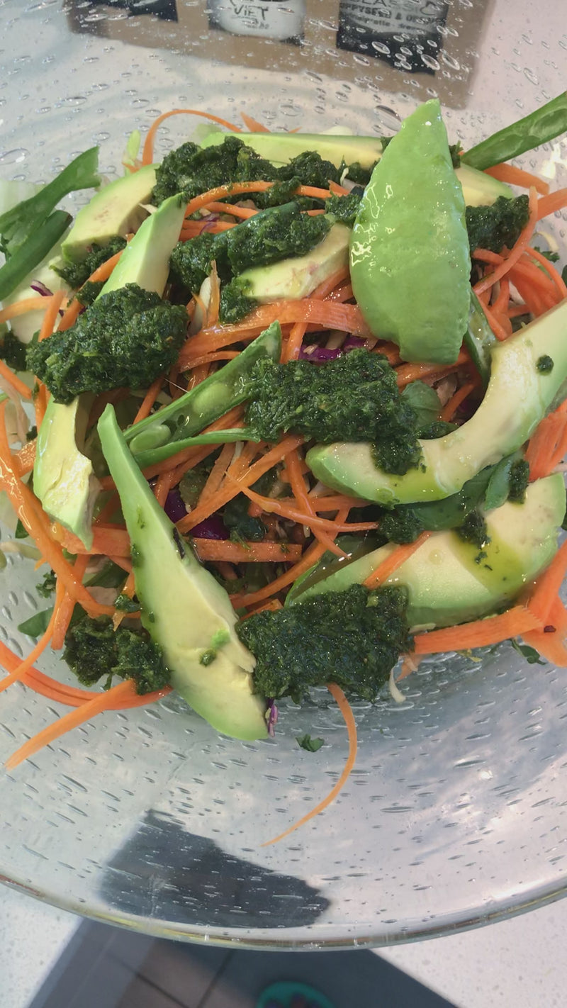 A demonstration of green herby sauce being generously drizzled over a fresh salad, enhancing its flavors with a burst of vibrant green goodness.