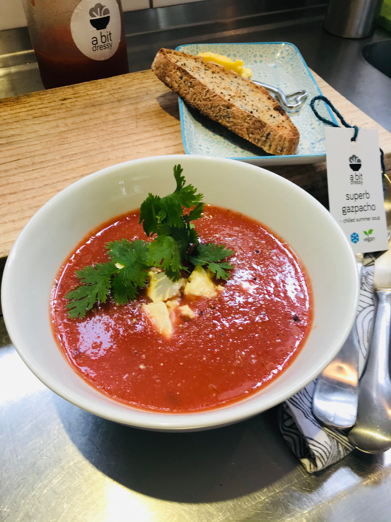 A fresh bowl of Superb Gazpacho Soup in a vibrant display on a table next to a slice of bread, offering a refreshing and appetizing meal.