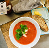 A bowl of Superb Gazpacho Soup placed on a table beside a slice of bread, creating a refreshing and delicious meal setup.