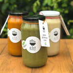 A glass jar filled with Green Goddess soup in the foreground, with two other glass jars of various soups in the background, offering a selection of delicious soup options