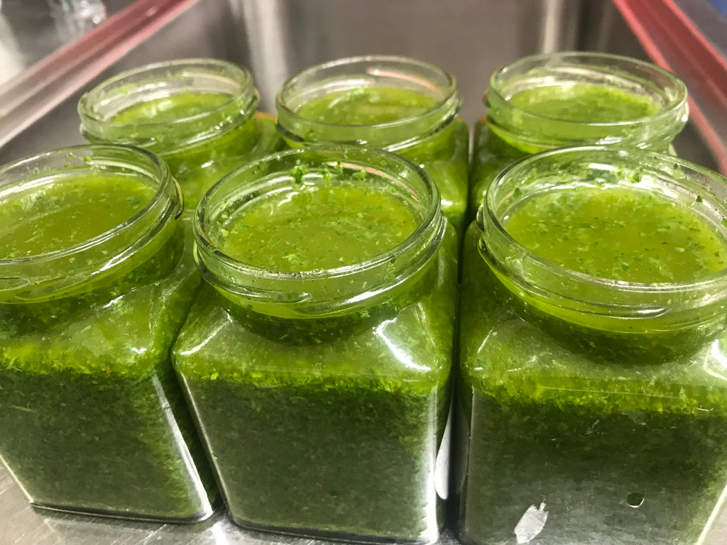 Jars filled with green herby sauce, featuring a vibrant and aromatic blend of fresh herbs and seasonings, perfect for adding flavor to a variety of dishes