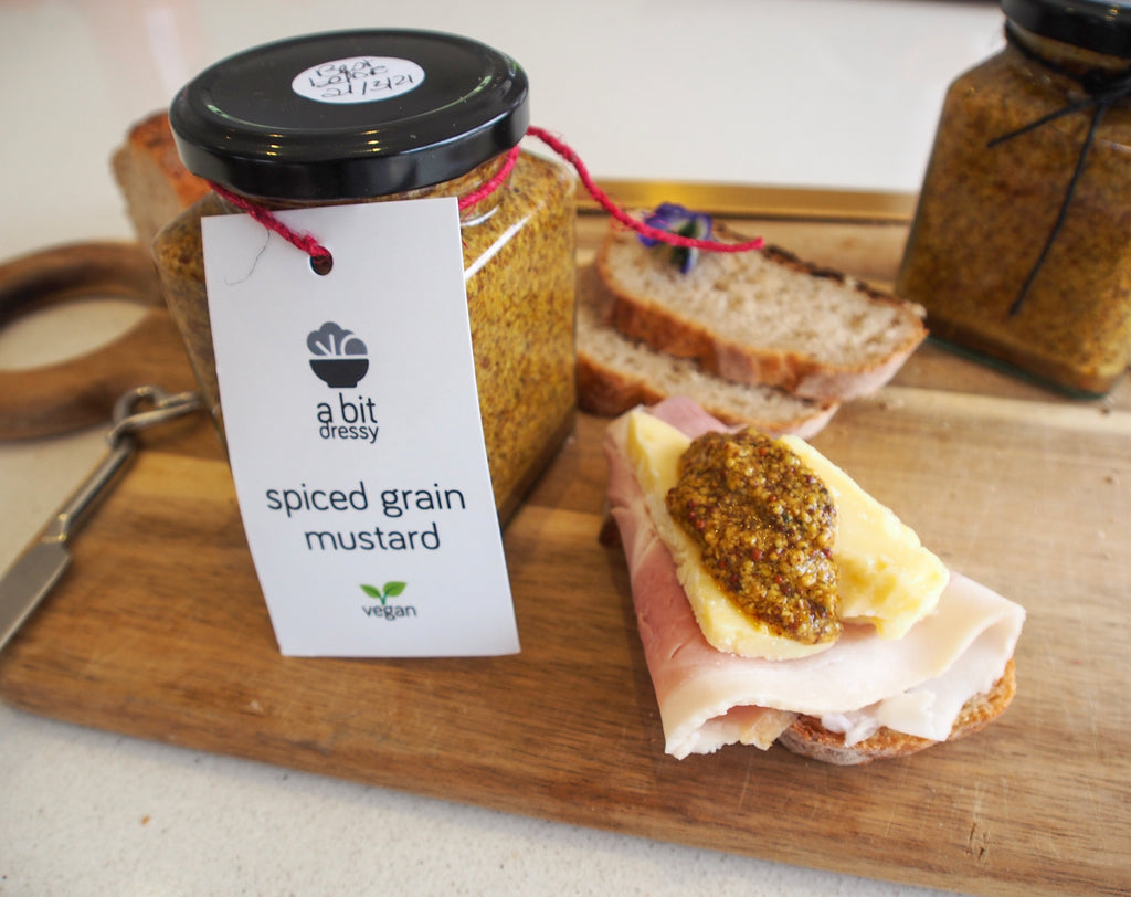 A jar of spiced grain mustard placed beside a sandwich, with the mustard spread inside, adding a flavorful and textured condiment to the sandwich