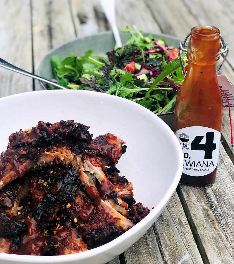 A table set with a bowl of ribs and a bowl of salad, accompanied by the Number 4 Kiwiana BBQ Sauce, creating a flavorful and satisfying meal.