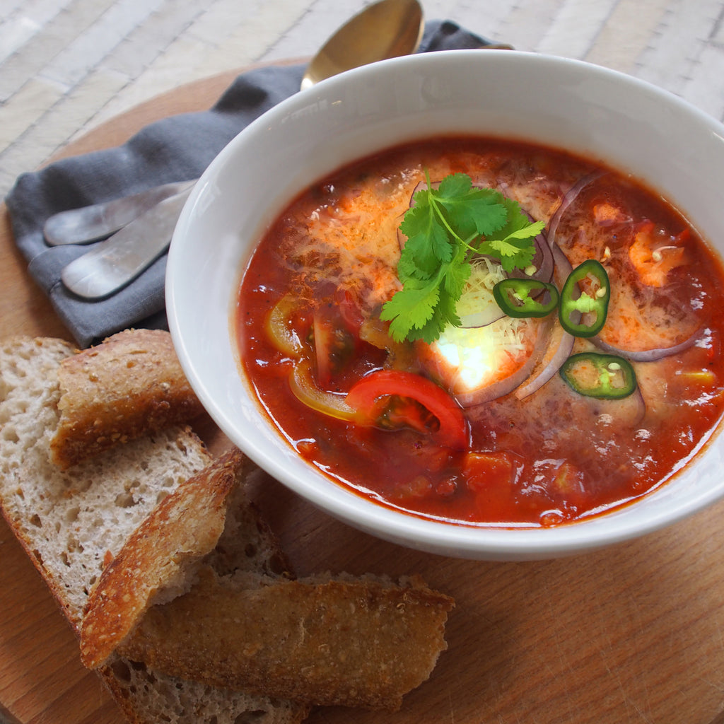 A bowl of spicy beef taco soup placed next to a slice of bread, offering a warm and hearty meal option.