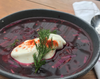 A glass jar filled with vegan borscht, featuring a vibrant, deep-red soup made from beets and other vegetables, with a dollop of dairy-free sour cream on top.